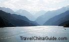 The small deep-blue Heavenly Lake is surrounded by hills covered with fir trees and grazed by horses.